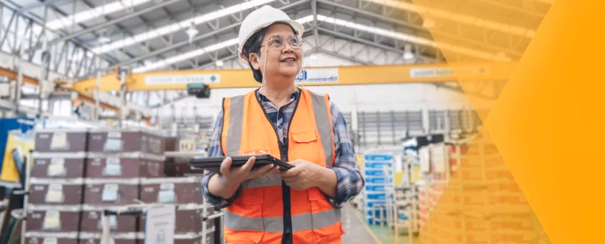 A person wearing a white hard hat and orange safety vest holds a tablet, checking frontline statistics while standing in a large warehouse or factory setting. Beekeeper