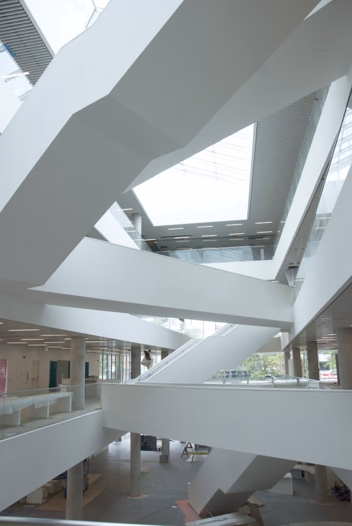 Modern multi-level interior with white angular staircases and skylight ceiling in public building.
