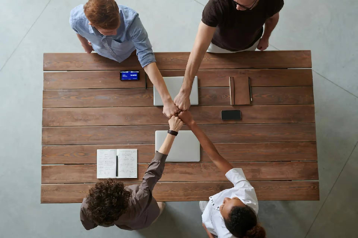 Four colleagues joining hands over a table, representing teamwork and a collaborative culture.