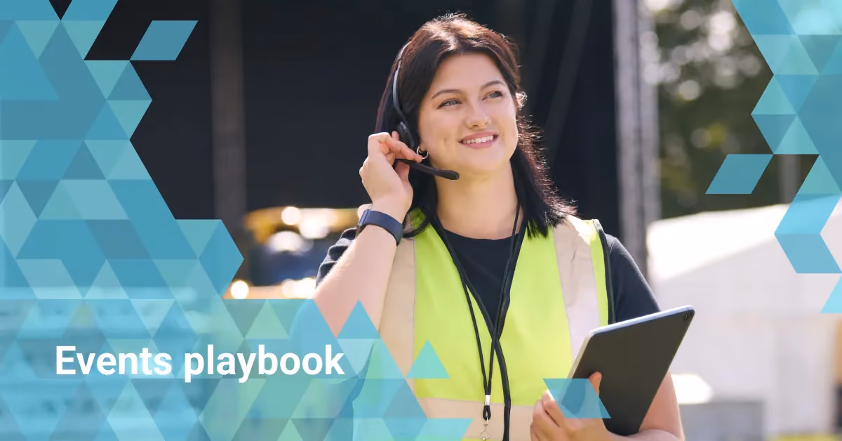 Smiling event staff wearing headset and neon safety vest holding a tablet outdoors.