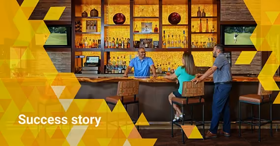 Bartender serving drinks to a man and woman at a bar with illuminated shelves and televisions.