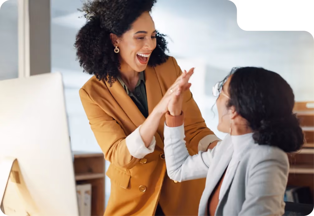 Two women smiling and giving a high-five in a bright office environment.