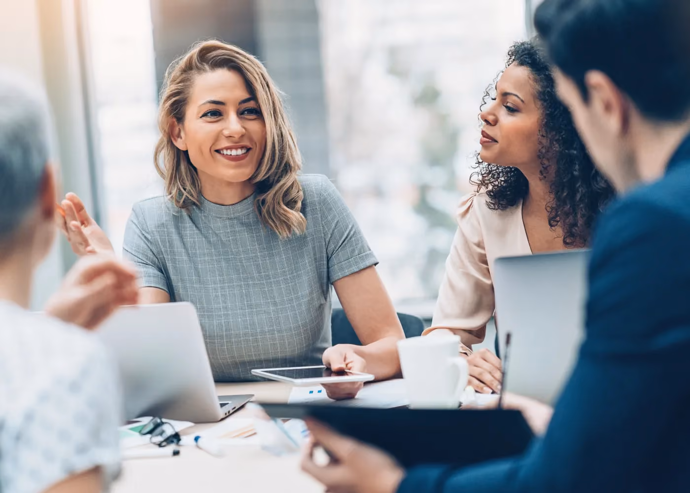 Four diverse professionals in a meeting, one woman smiling and speaking with a tablet in hand.
