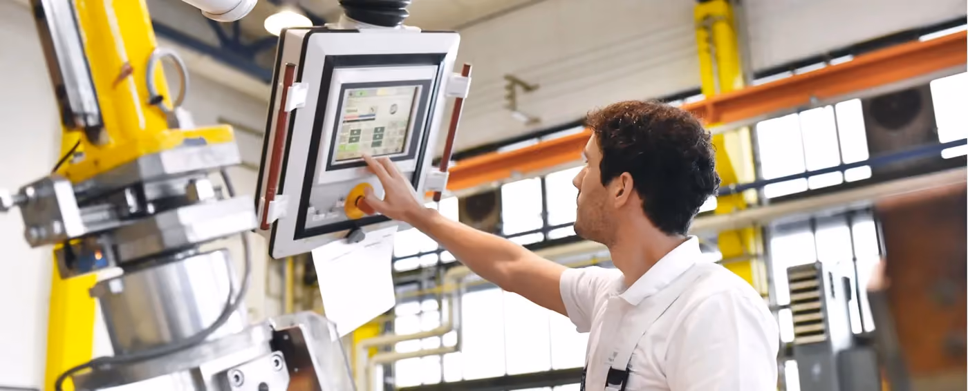 Man operating a control panel on industrial machinery inside a factory setting with yellow beams.