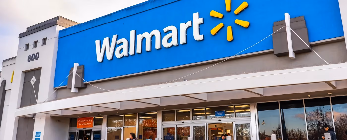 Exterior of a Walmart store with blue signage and people entering through glass doors.
