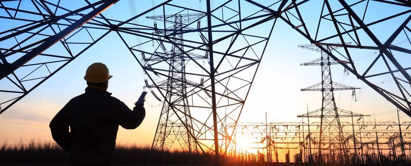 Electric power engineer with hard hat inspecting transmission towers at sunset with blue sky background.