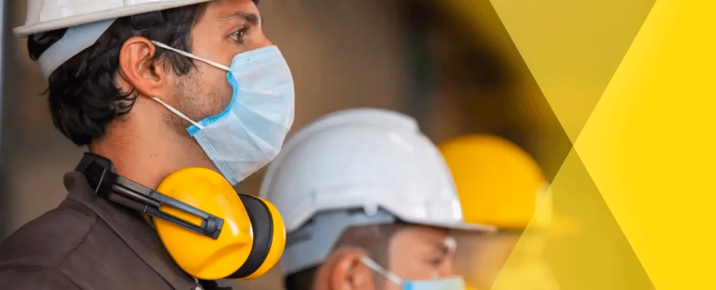 Workers wearing safety helmets, face masks, and yellow ear protection at a work site.