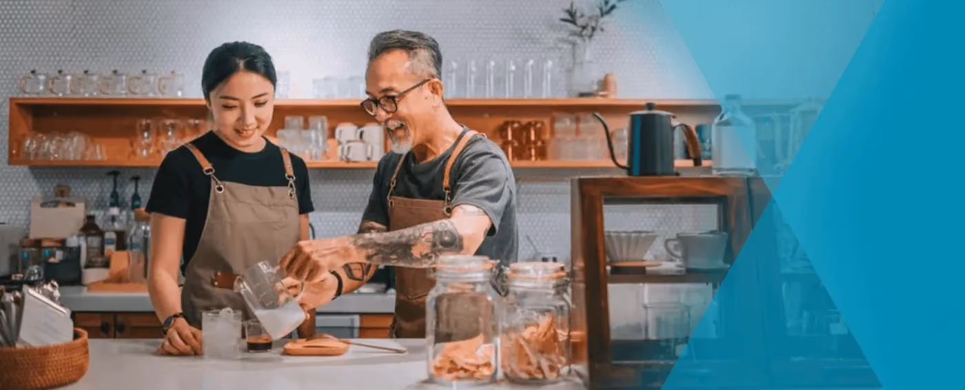 Two baristas in aprons preparing coffee behind a counter in a modern cafe setting.