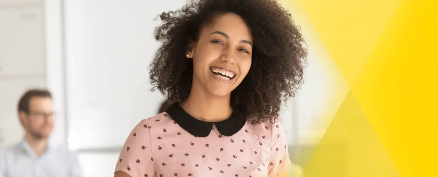 Smiling woman with curly hair wearing a pink shirt with black collar in office setting.