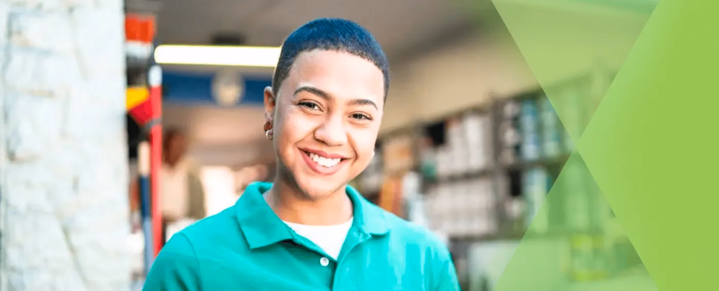 Smiling young person in a green polo shirt standing in an indoor setting with shelves in background.