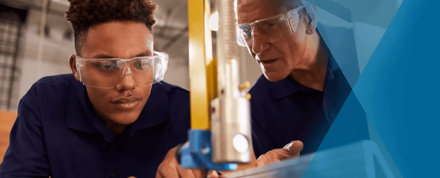 Two men wearing safety glasses focused on a machine tool in an industrial setting.