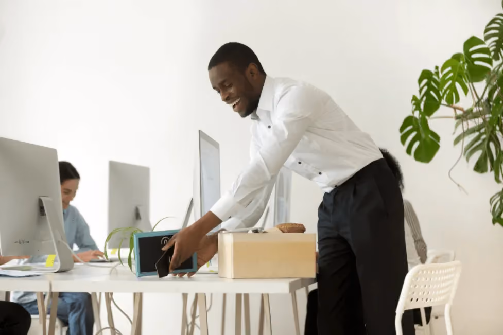 Smiling man in white shirt placing a phone near a blue device on a white office desk.