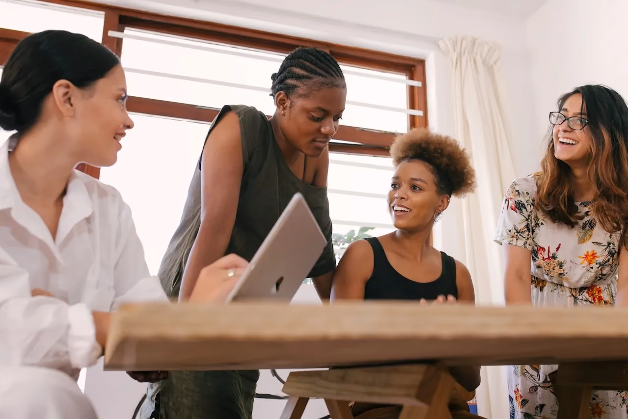 Four women engaged in a lively discussion around a wooden table in a bright room.