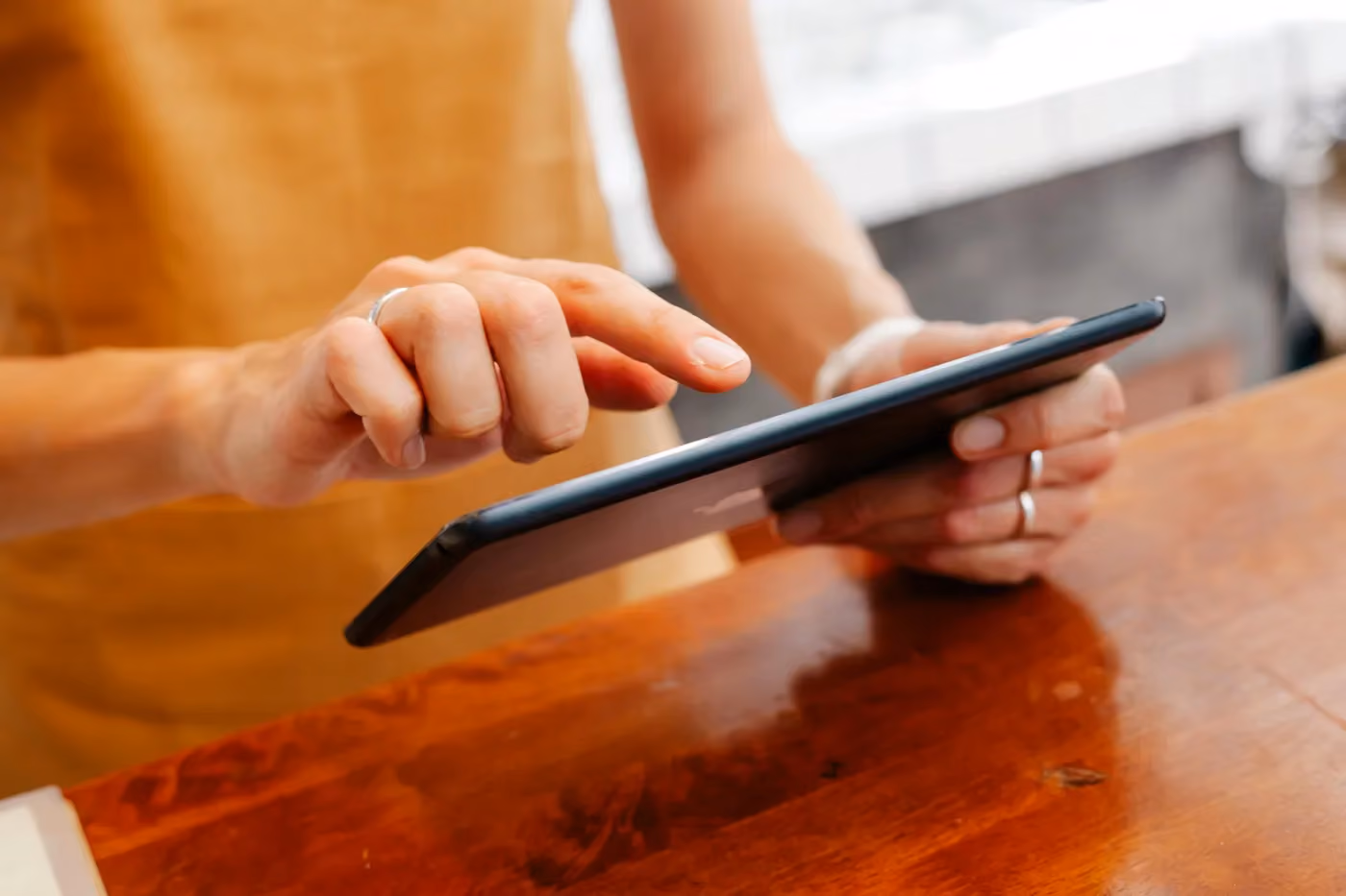 Person using fingers to tap and hold a tablet device over a wooden table.
