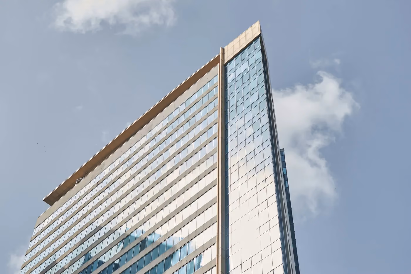 Modern skyscraper with reflective glass facade against a clear sky with scattered clouds.
