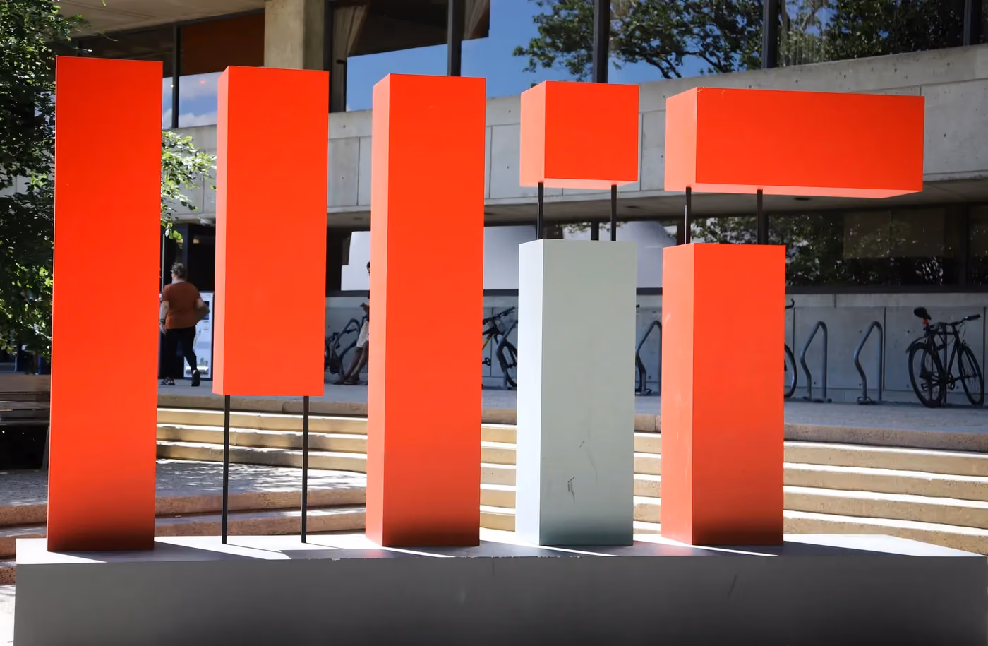 Modern outdoor sculpture of tall red rectangular shapes and one white block on a platform.
