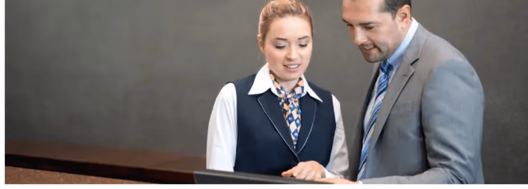 Hotel receptionist and a guest looking at a computer screen at the front desk.