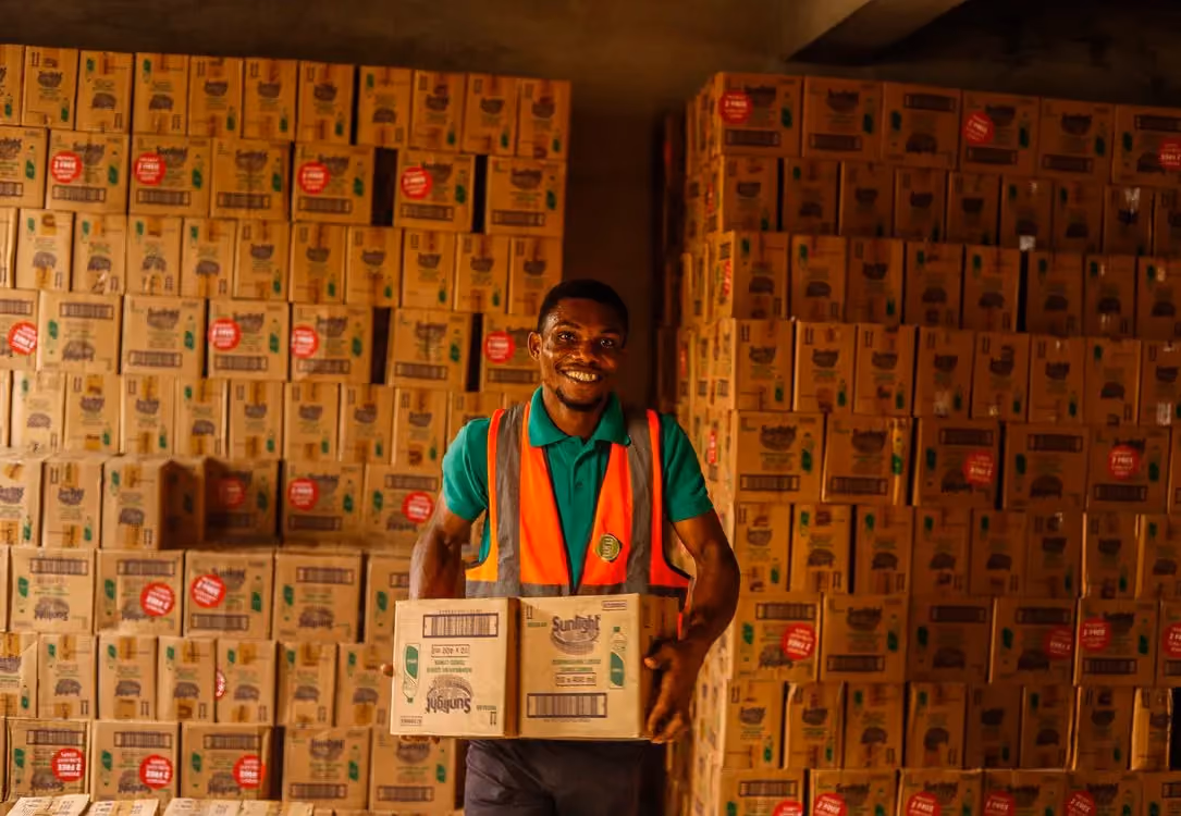 Smiling frontline warehouse worker in a safety vest holding boxes in natural sunlight