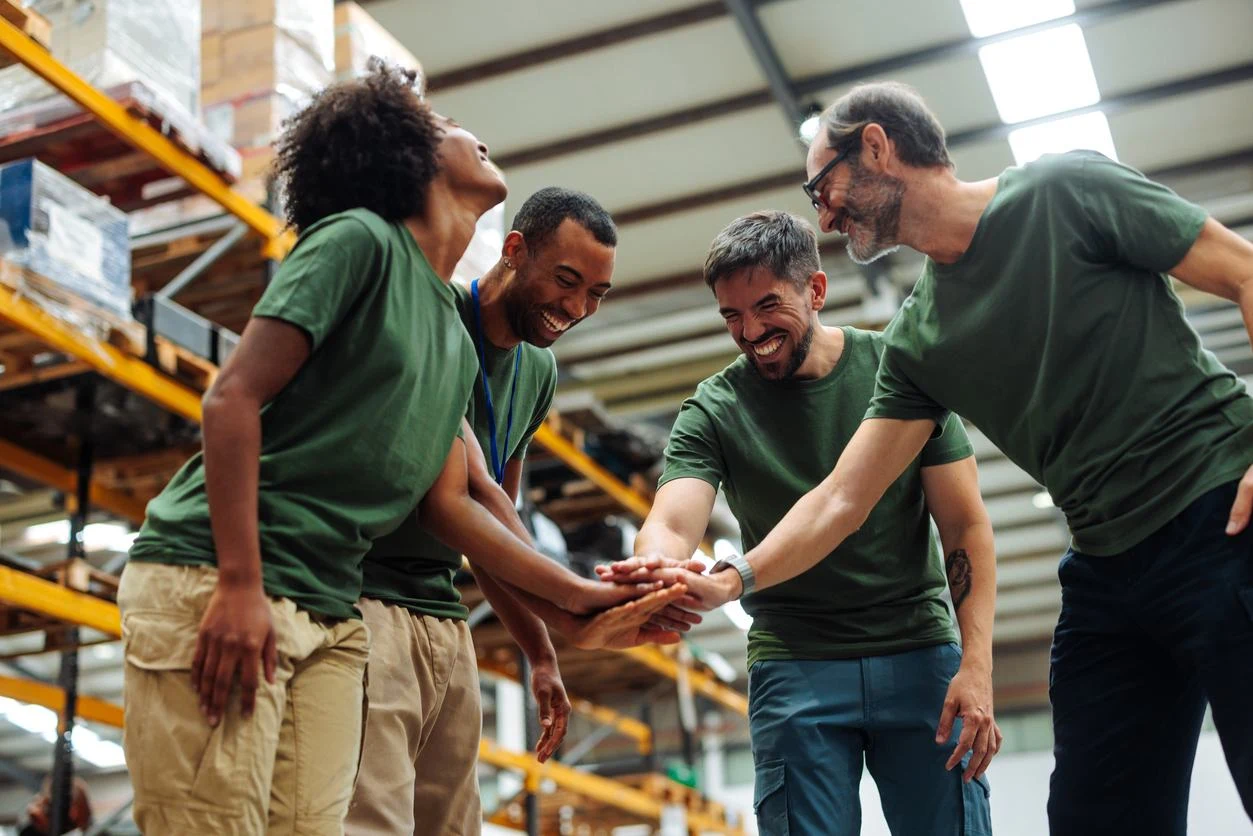 Colleagues in a warehouse putting their hands together in a team huddle