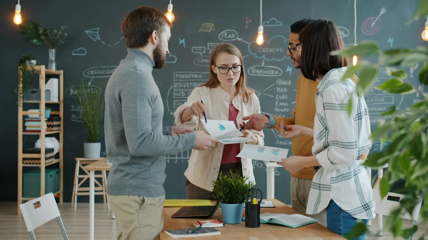 Four colleagues review printed reports together at a table in a bright office, agreeing how shared knowledge is organized.