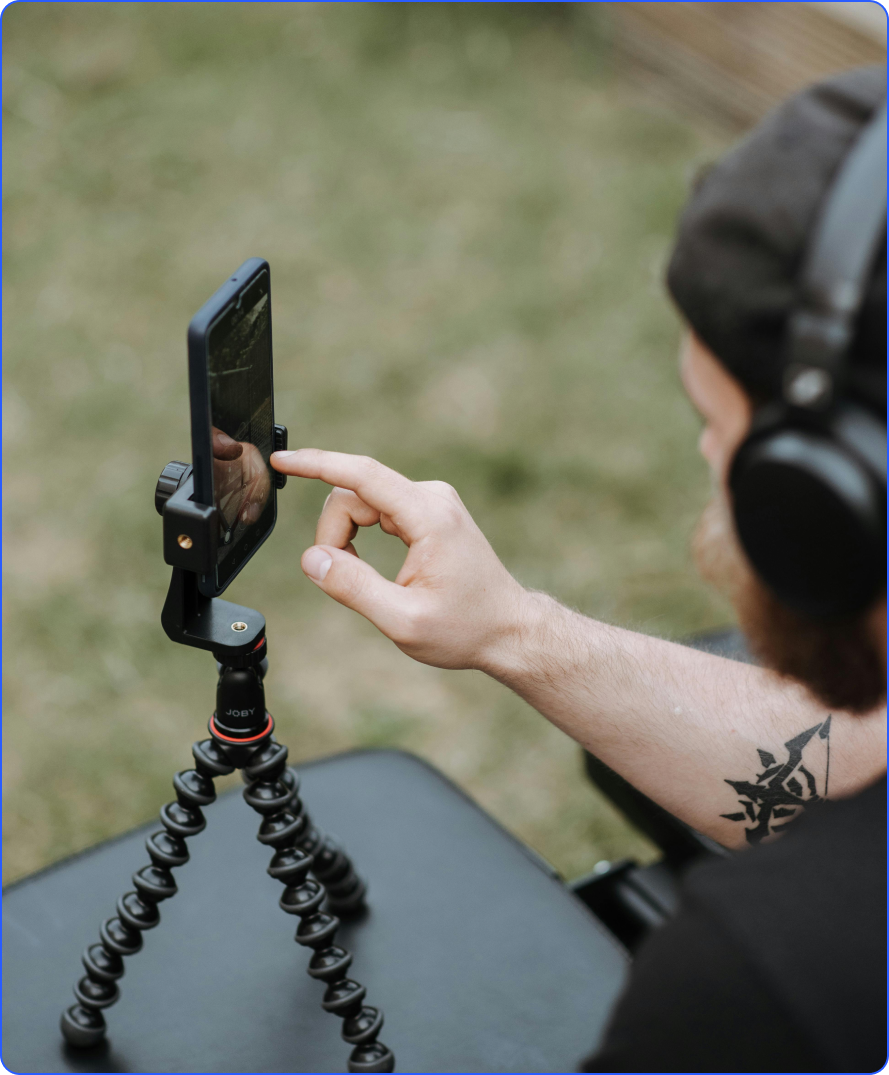 Person wearing headphones using a smartphone mounted on a Joby flexible tripod outdoors.