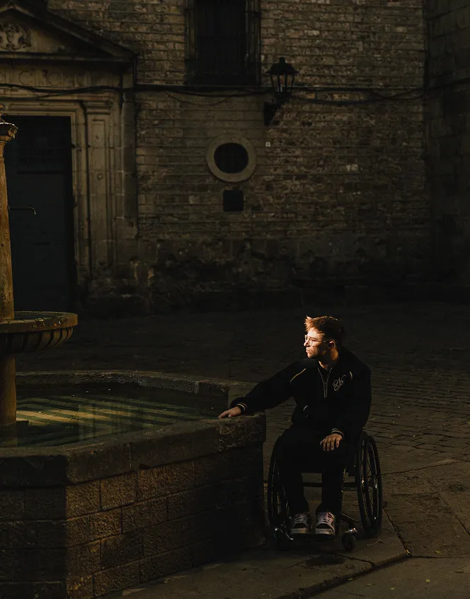 Jonas Bell en chaise roulant au coin d'une ancienne fontaine en pierre.
