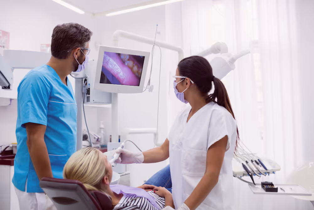 A dentist and dental assistant examine a patient's teeth using a screen display in a dental clinic.