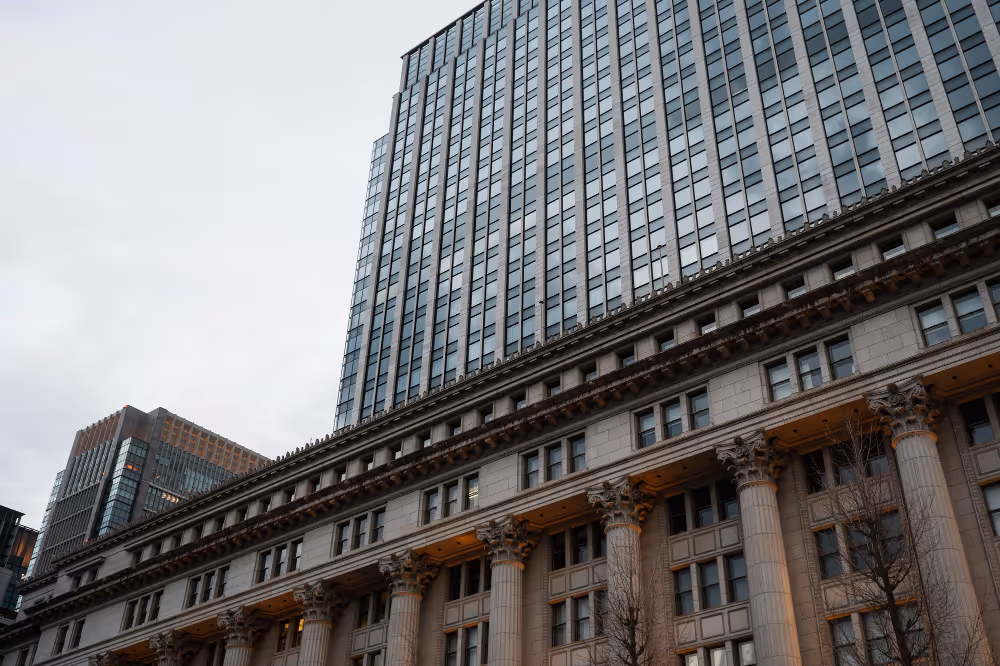 Tall office building with large columns and numerous windows under a cloudy sky.