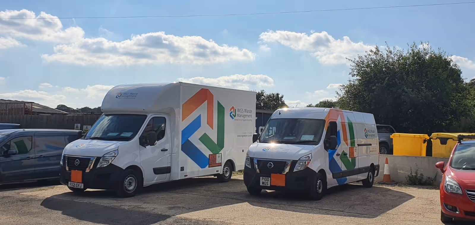 Two white delivery vans with colorful logos parked side by side in a sunny lot.