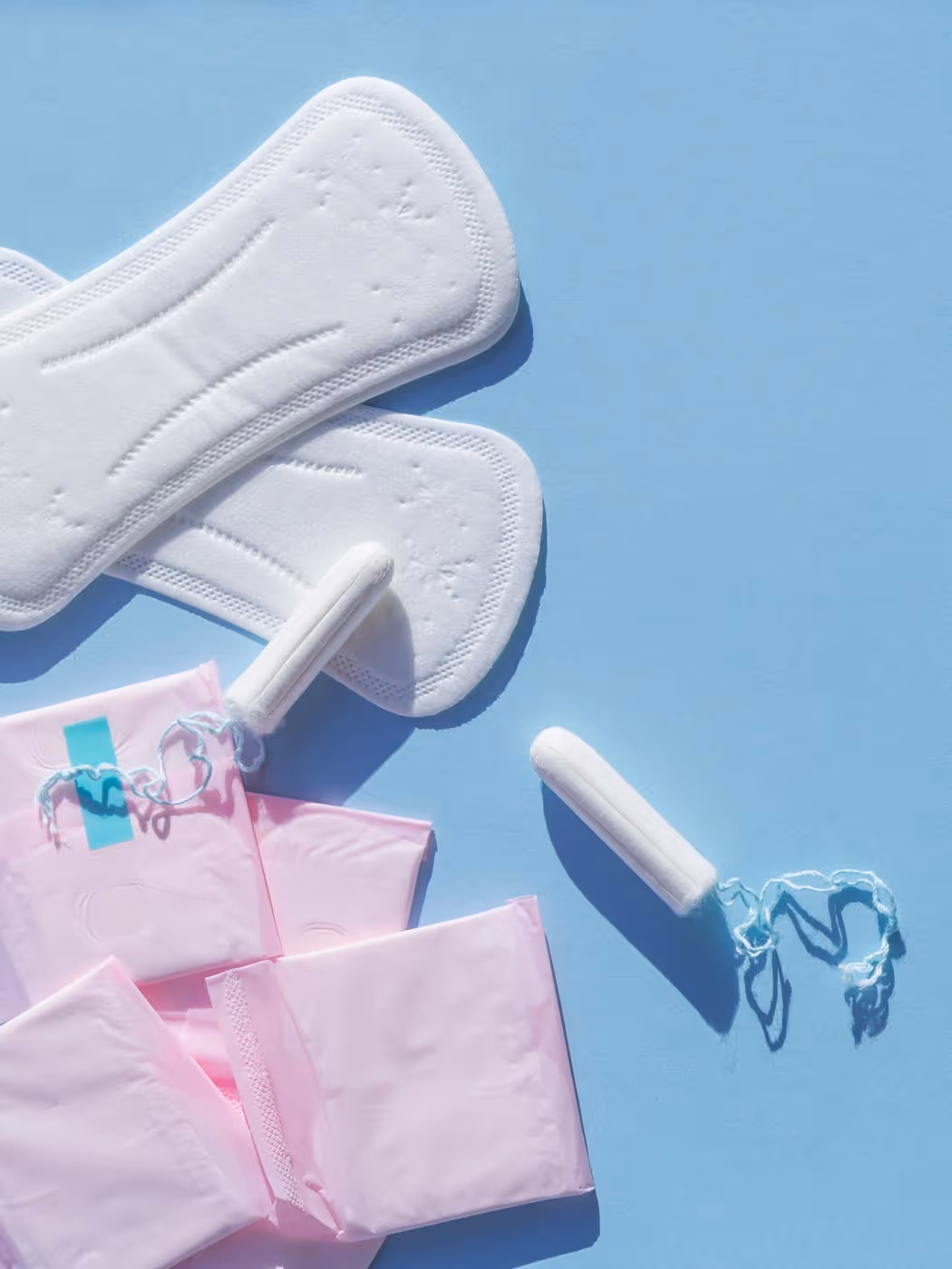 Tampons and sanitary pads arranged on a blue surface.