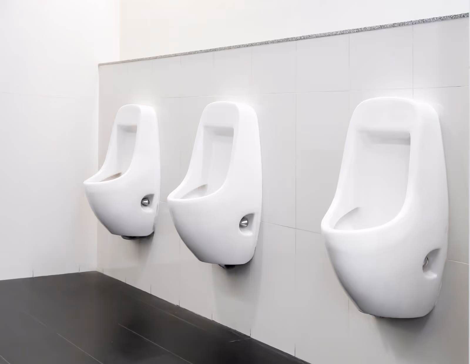 Three white urinals mounted on a tiled wall in a public restroom.