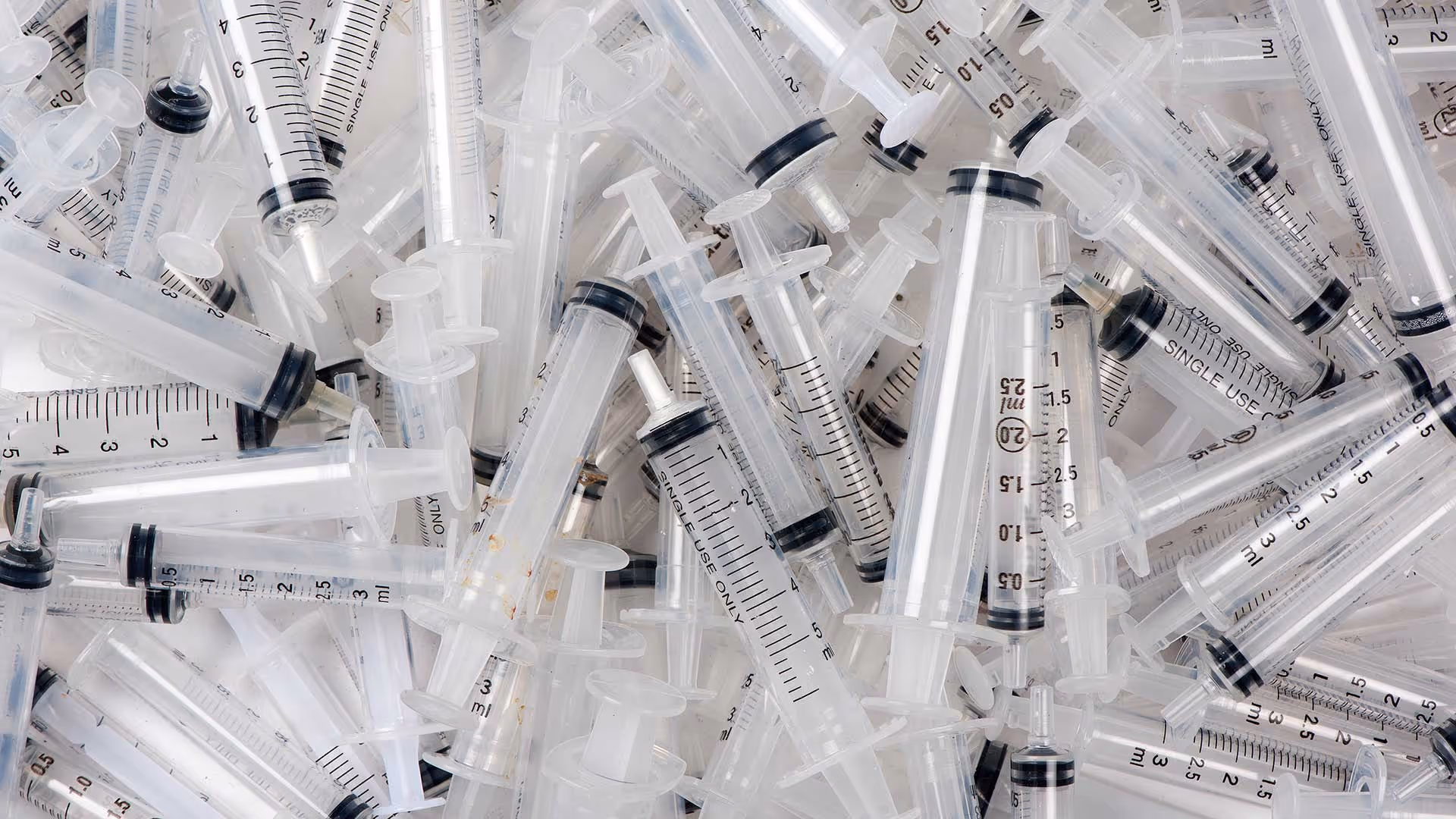 Pile of empty syringes with clear plastic barrels and black plunger tips scattered randomly.