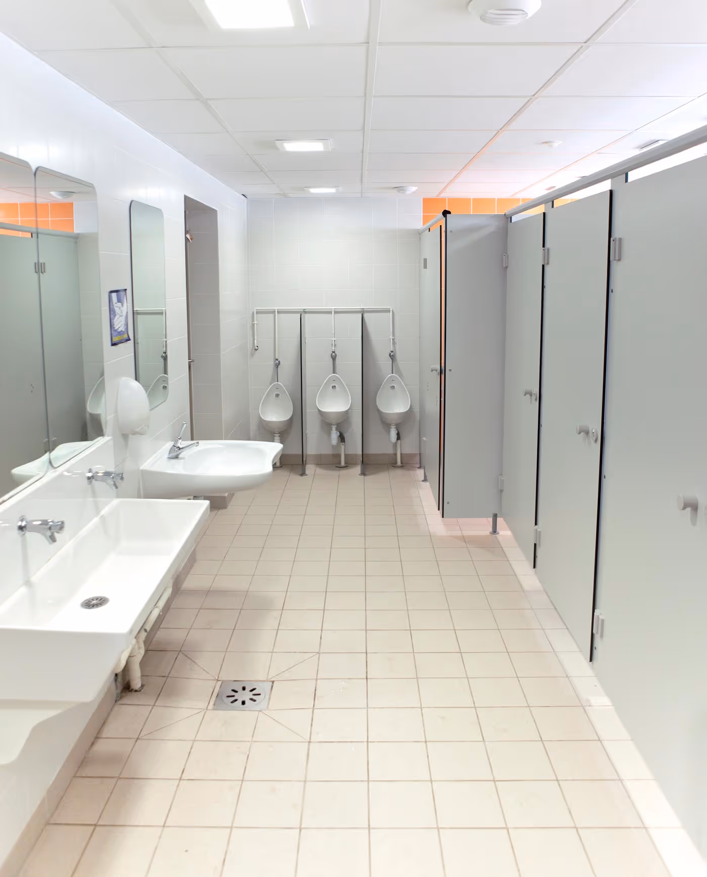 Public bathroom with sinks, urinals, and closed stall doors visible.