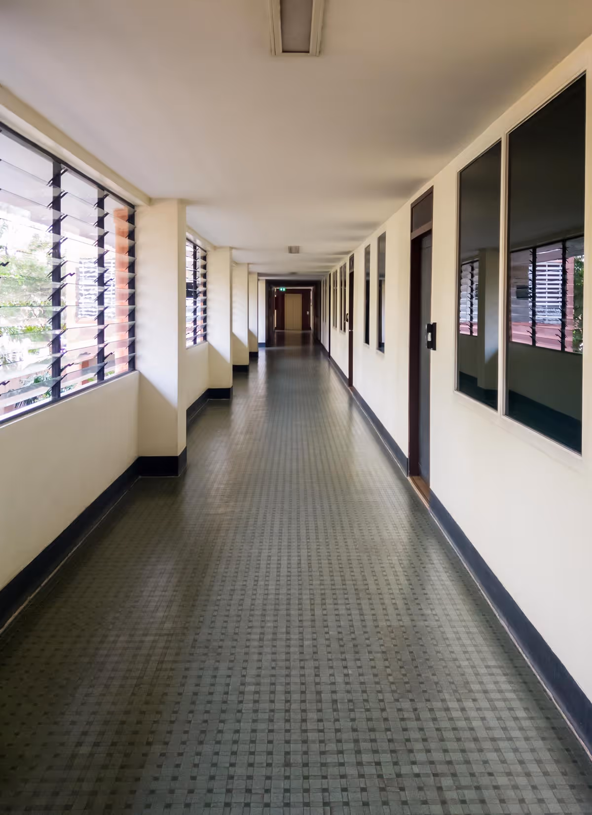 A long, empty hallway with white walls and green checkered floor tiles.