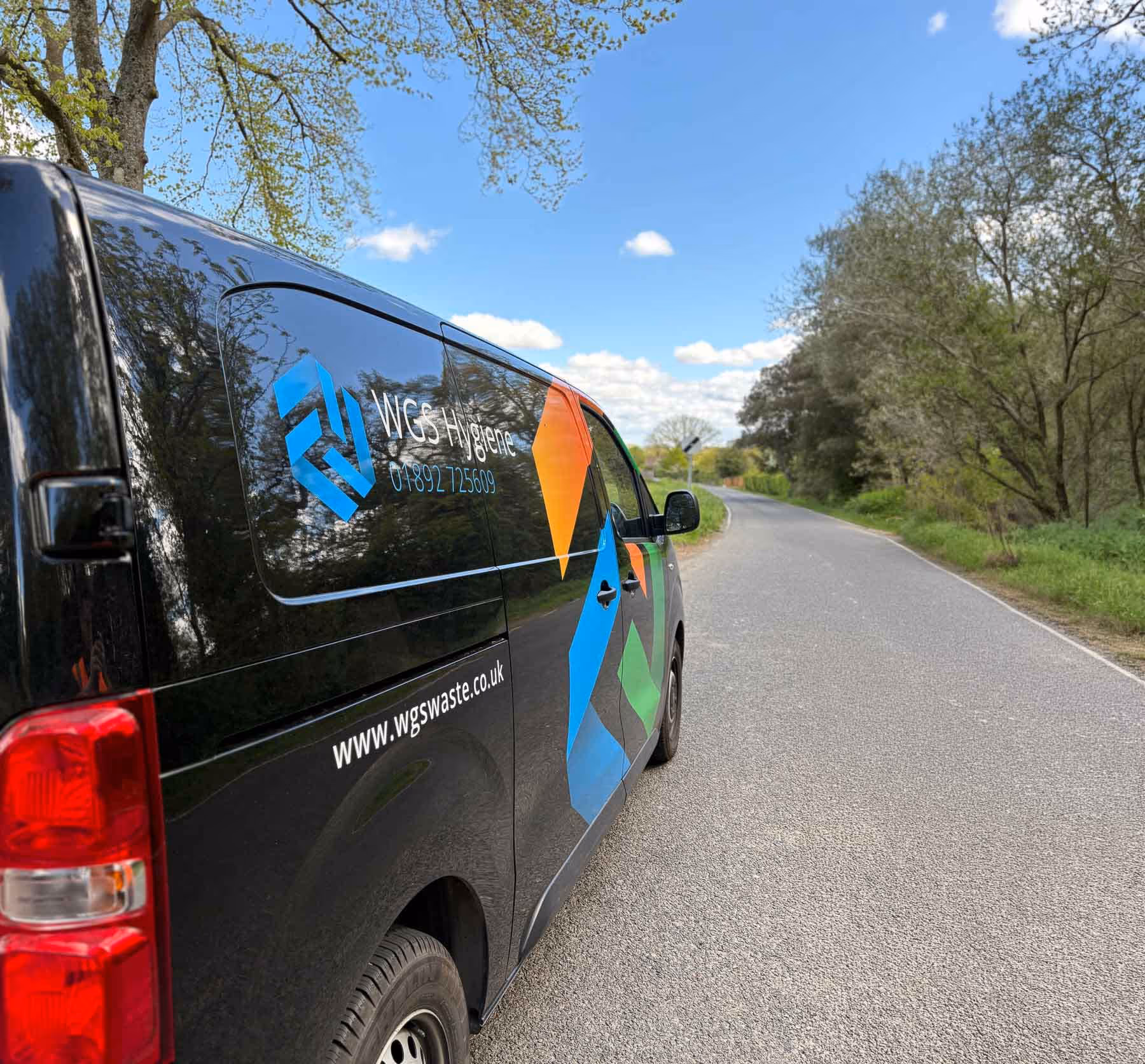 A black van with colorful logos is parked on a rural road under a clear blue sky.
