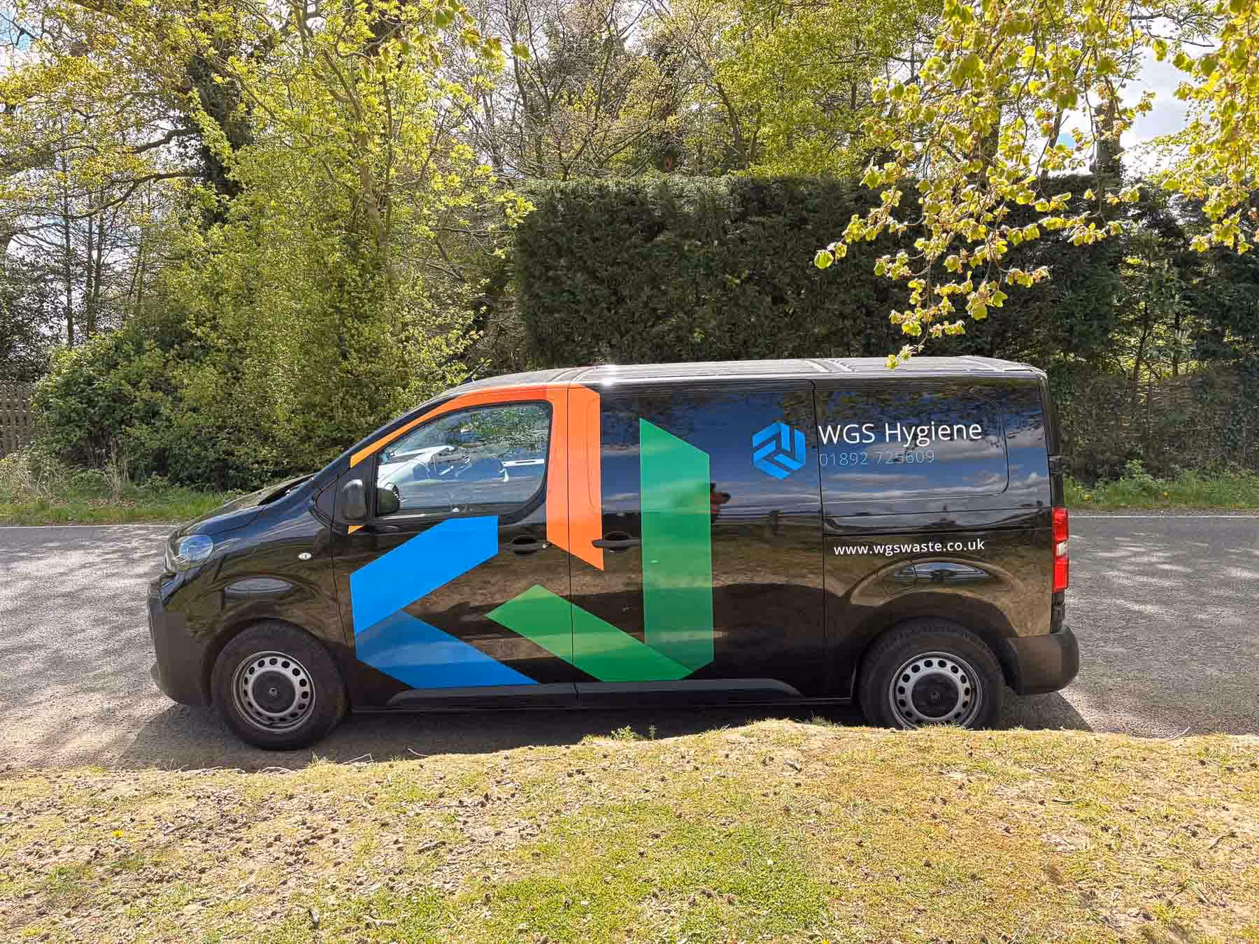 A black van with colorful logos and "WGS Hygiene" written on the side is parked on a road.