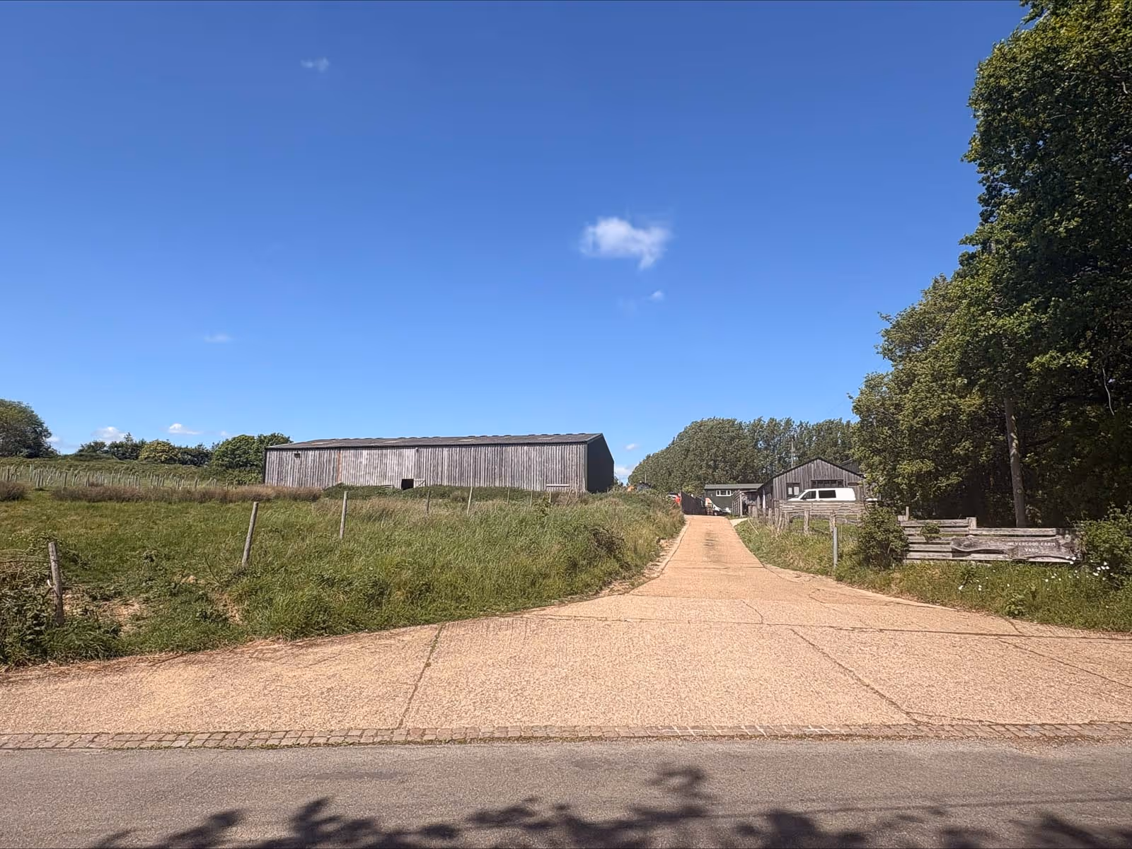 A gravel road leads to farm buildings with grassy fields and a clear blue sky.