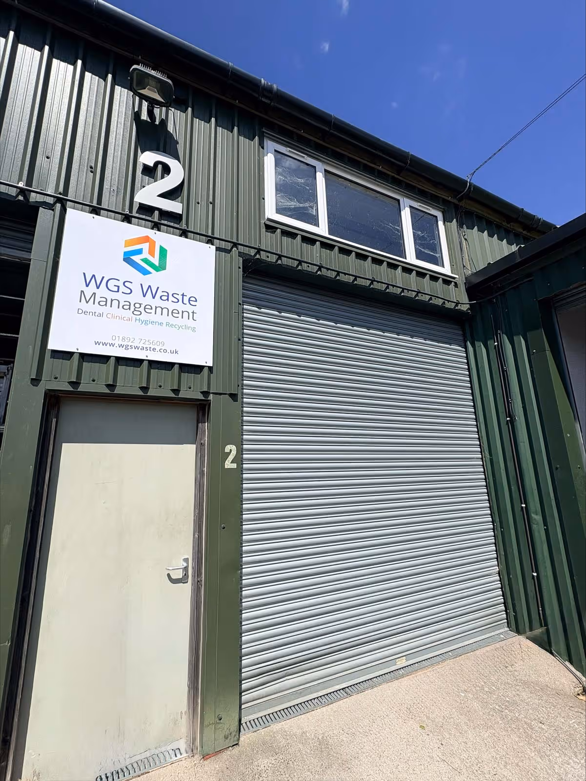 A green industrial building with closed roller door and a sign reading "WGS Waste Management" above the door.