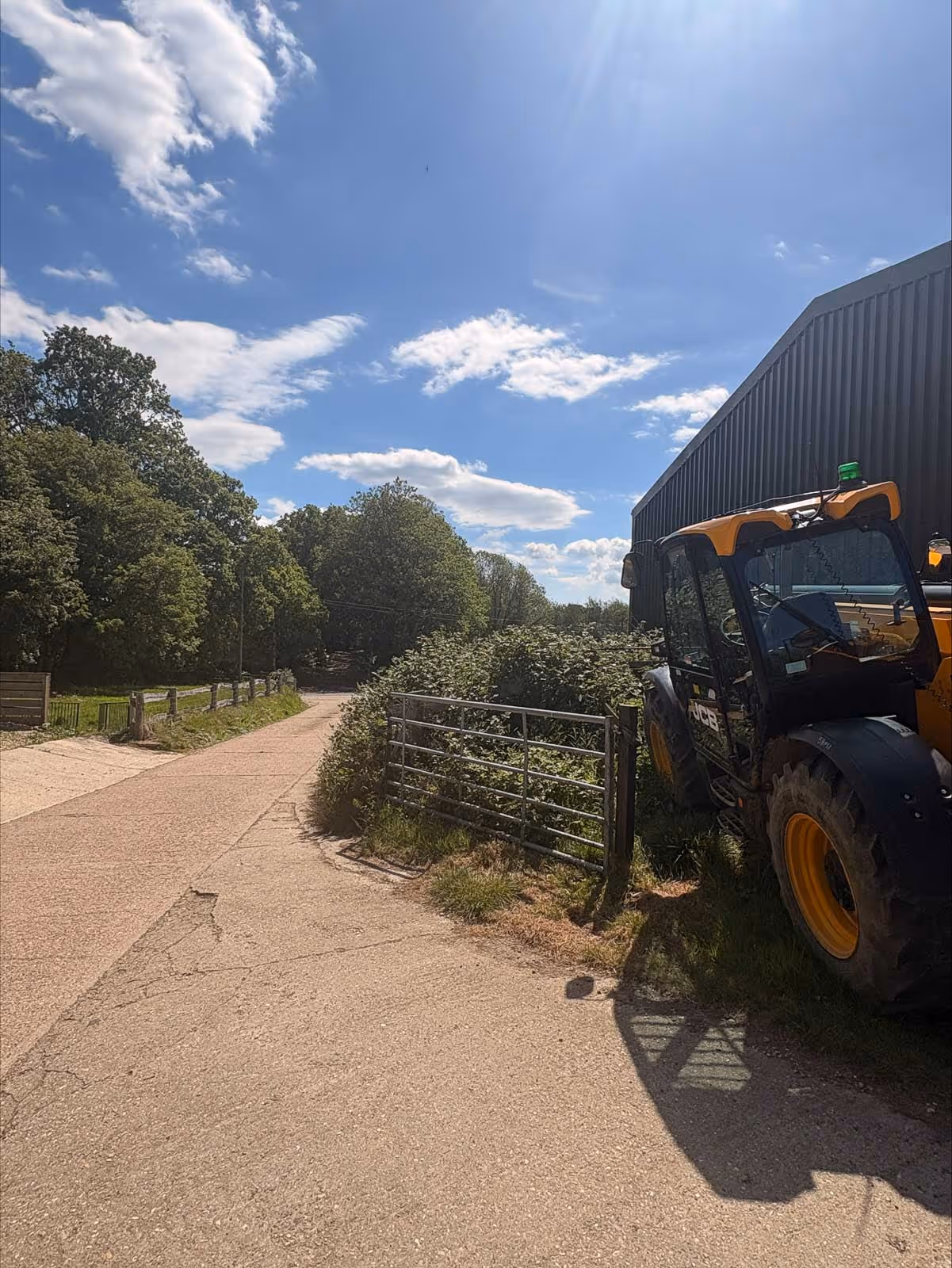 A tractor is parked next to bushes near a large metal building on a sunny day.