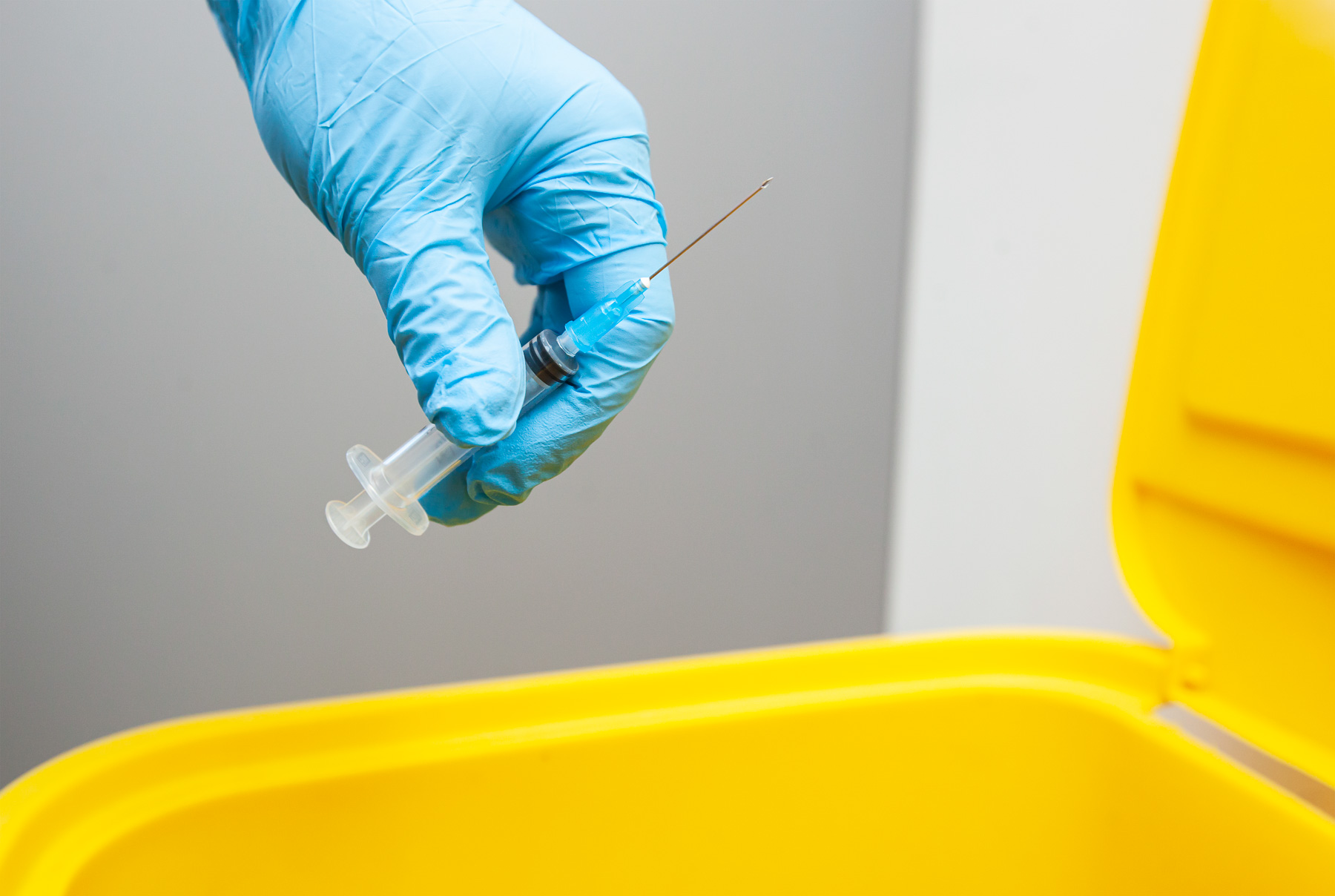 Gloved hand disposing of a used needle into a sharps bin