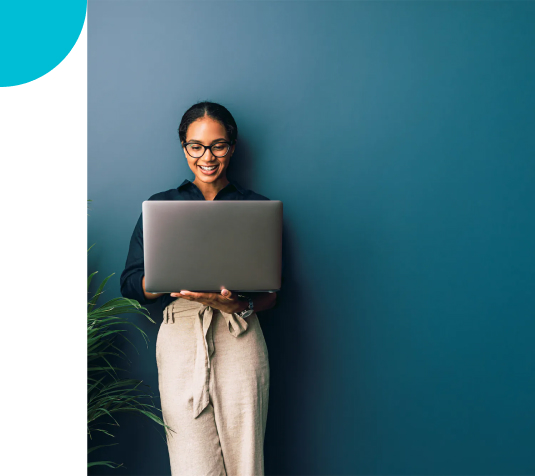 A smiling woman holding a laptop in front of a blue wall