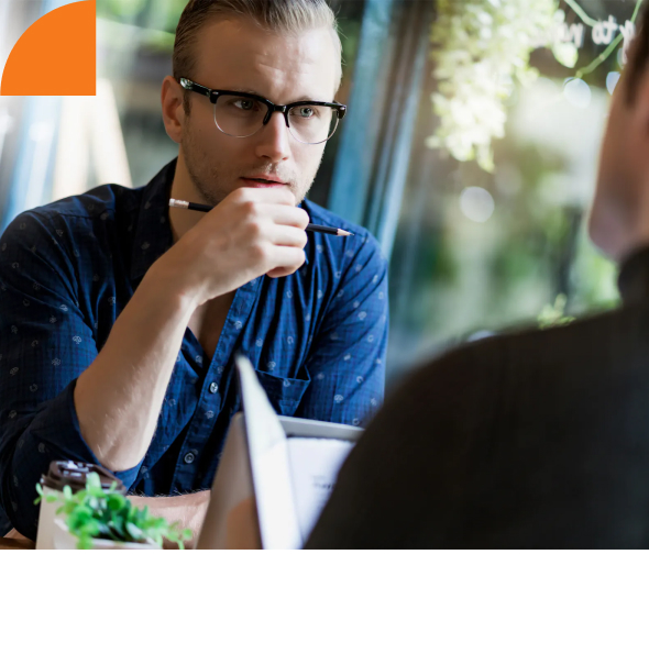 A man with glasses sitting at a table talking to another man