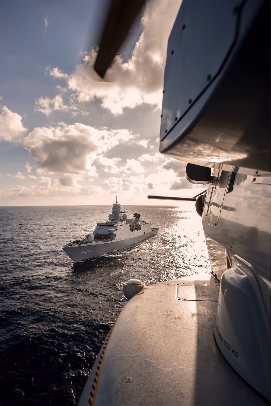 Marineschip op zee gezien vanuit een ander marineschip onder een gedeeltelijk bewolkte lucht.
