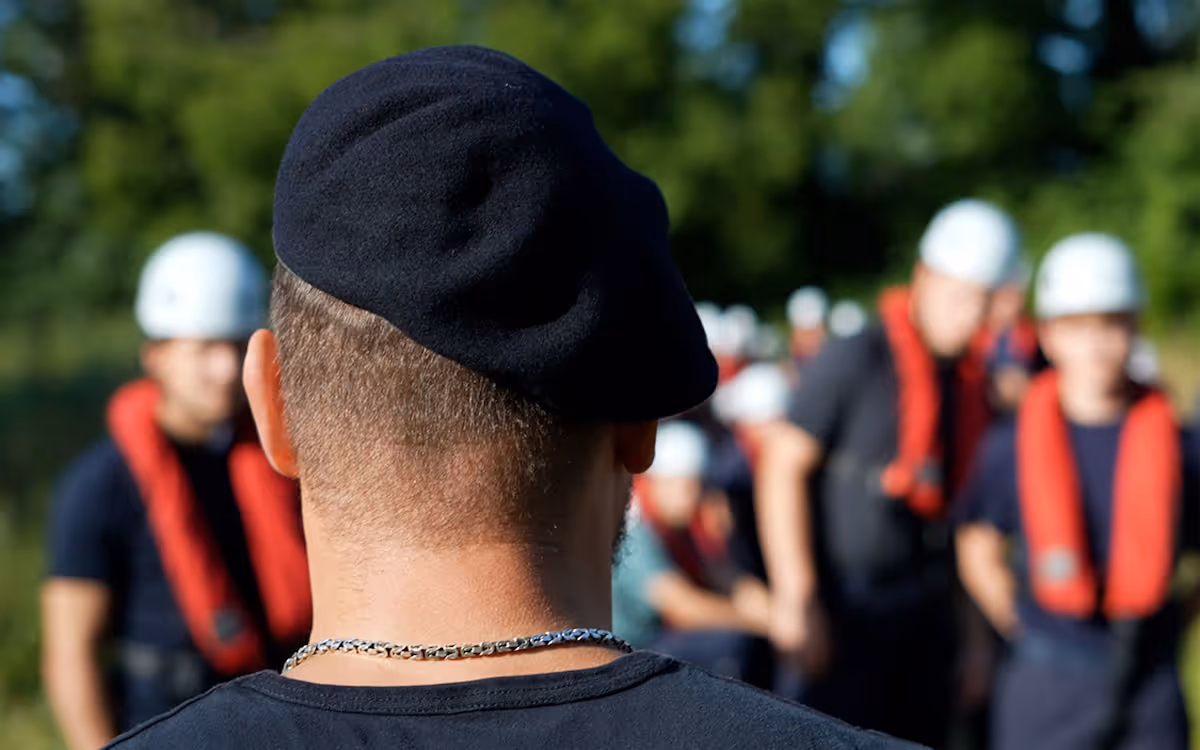Marine-instructeur met zwarte baret kijkt naar groep mannen in veiligheidsharnassen en helmen.