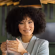 Smiling woman with curly hair holding a cup while sitting indoors.