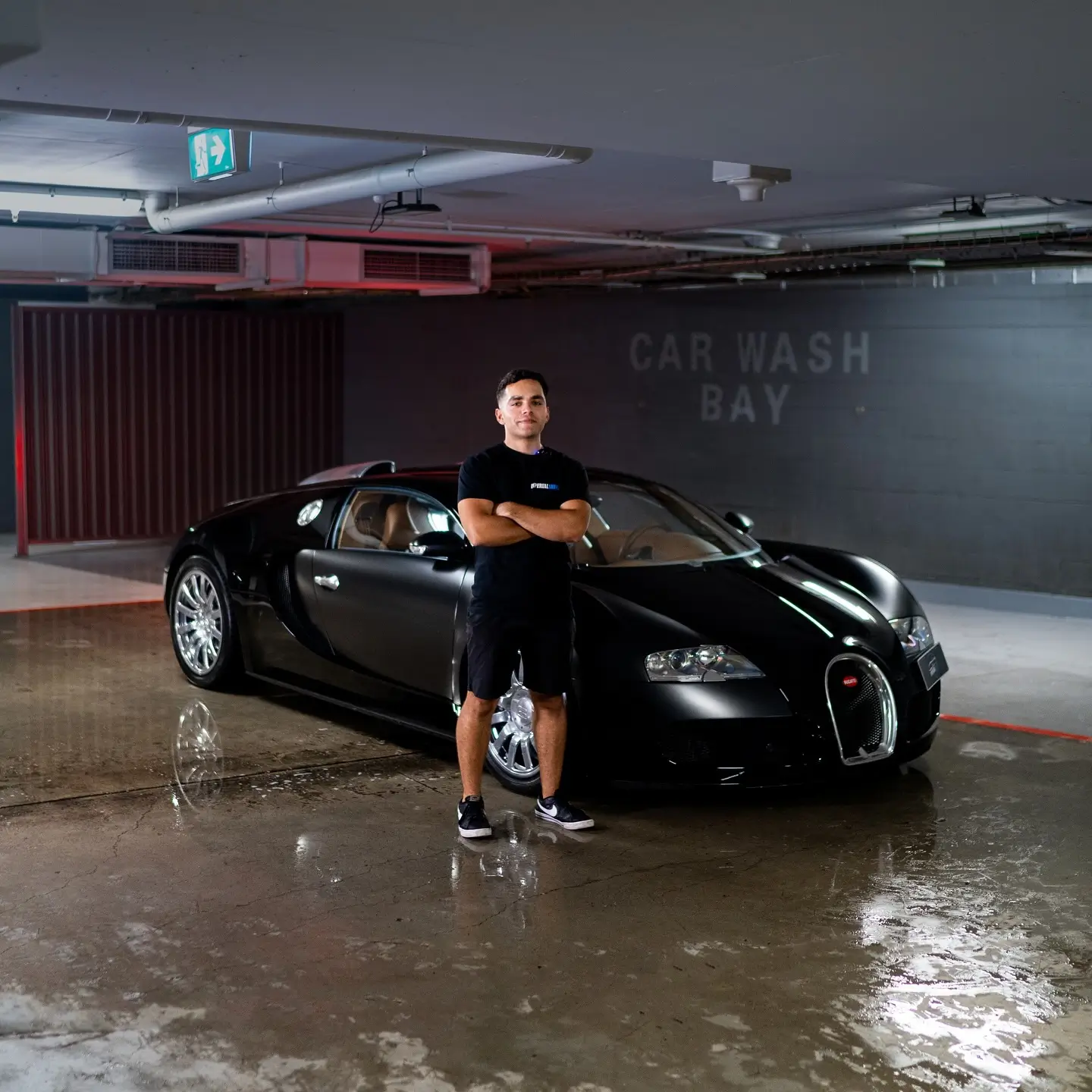 Professional standing beside a Bugatti Veyron during a premium detailing service in a car wash bay