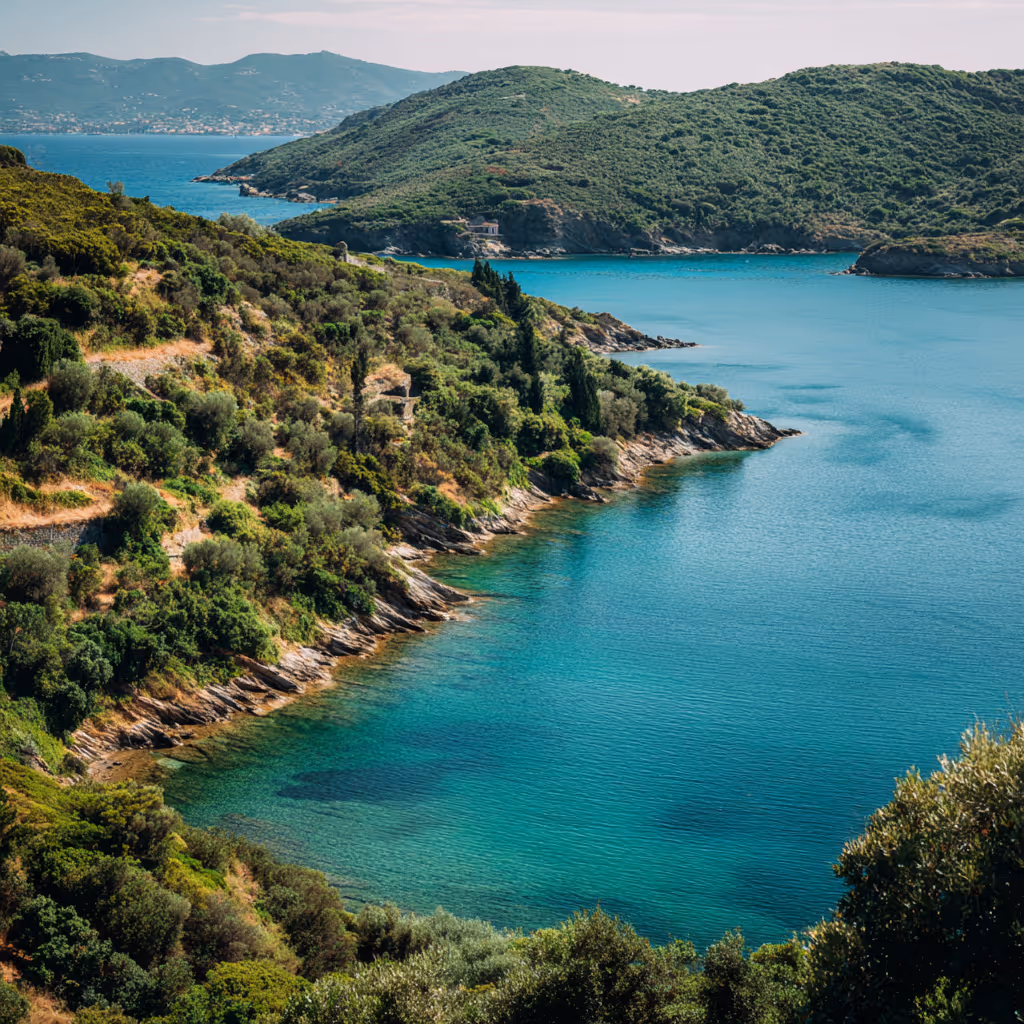 Clear blue coastal waters bordered by lush green hills and rocky shorelines under a partly cloudy sky.