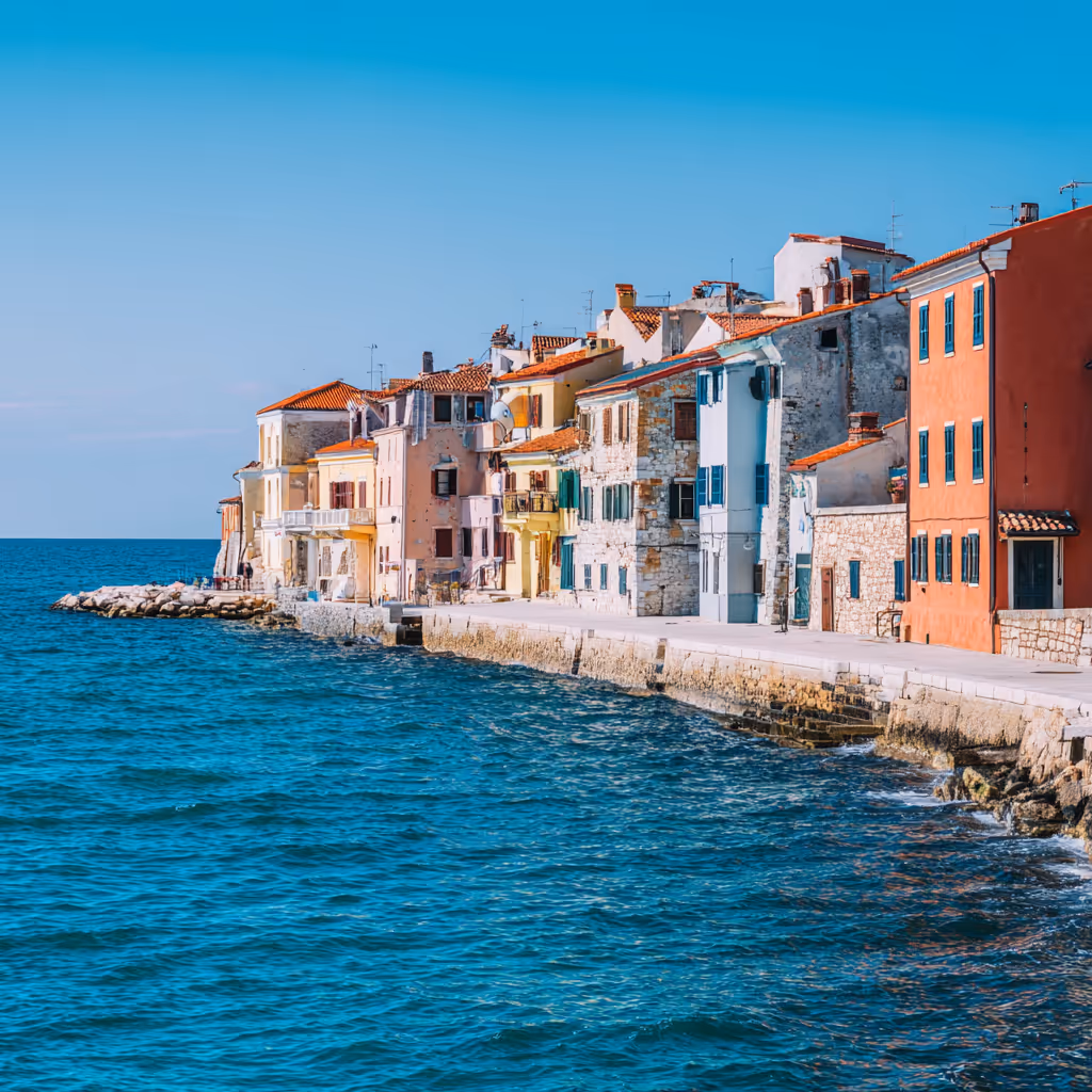 Colorful seaside buildings along a stone waterfront with clear blue sea under a bright sky.
