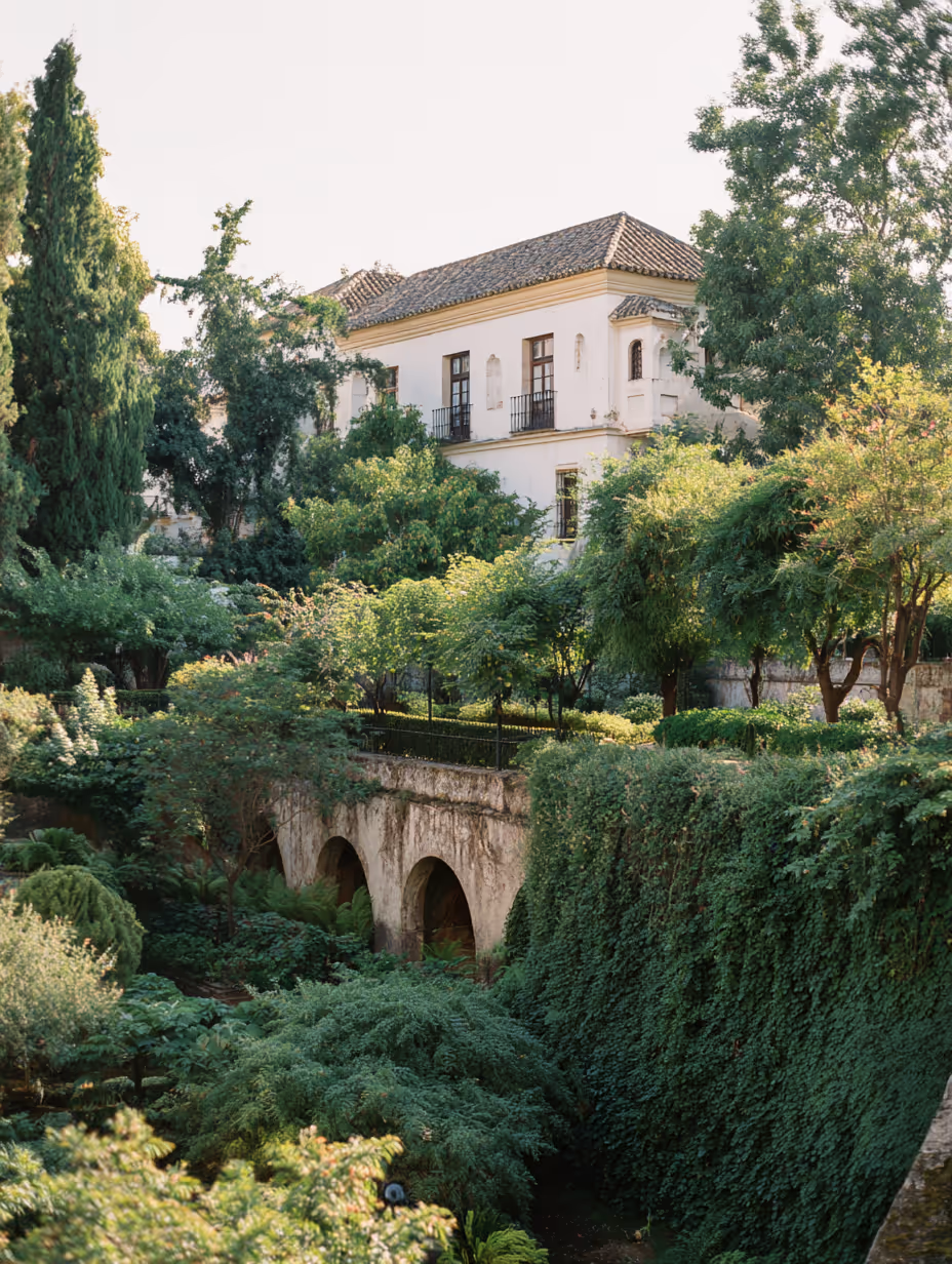 Historic white building with tiled roof surrounded by lush green trees and dense foliage.
