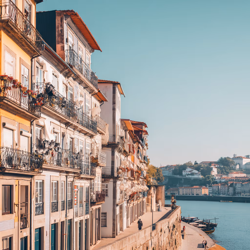 Oude gebouwen met balkons langs een rivierpromenade aan het water in een historische Europese stad bij helder weer.